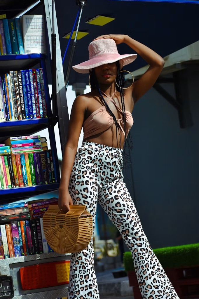 A woman in a pink hat and leopard pants standing by a shelf of books